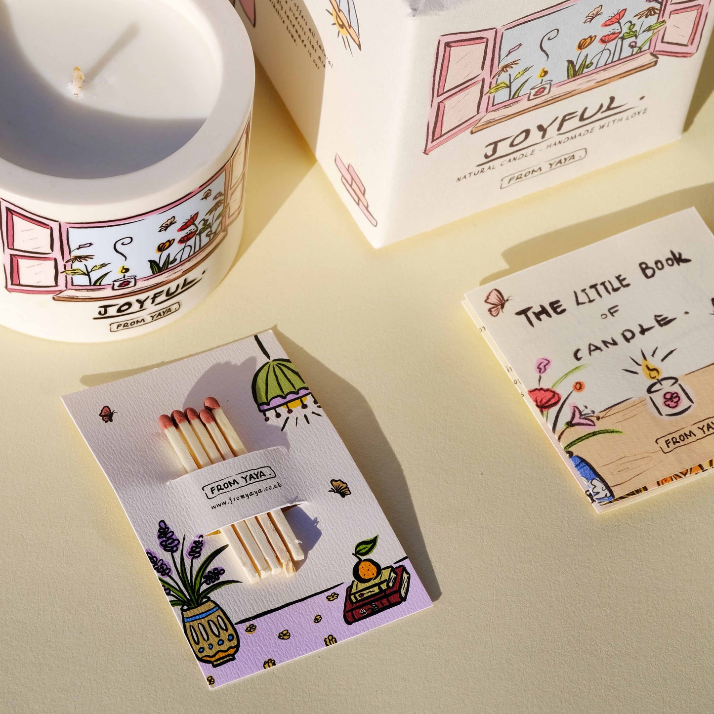Close up of Joyful essential oil candle with packaging, matches and the little book of candle descriptive book. All illustrated with cute, personal designs.